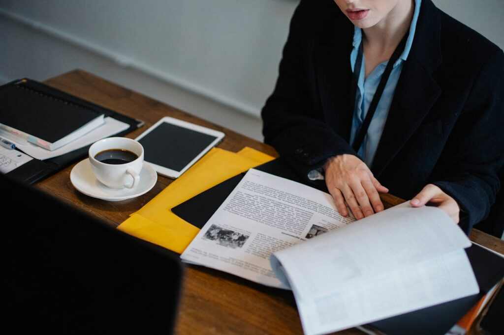 High angle of crop faceless businesswoman in formal clothes sitting at table with tablet and hot coffee and looking through documents