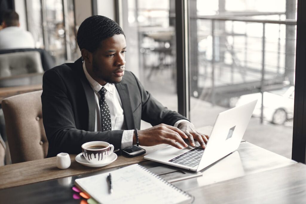 Adult man in a suit using a laptop at a café table with coffee.